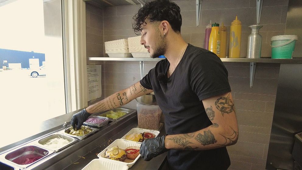 Daniel i sin restaurangvagn i Umeå när han fyller matlådor med hamburgare.