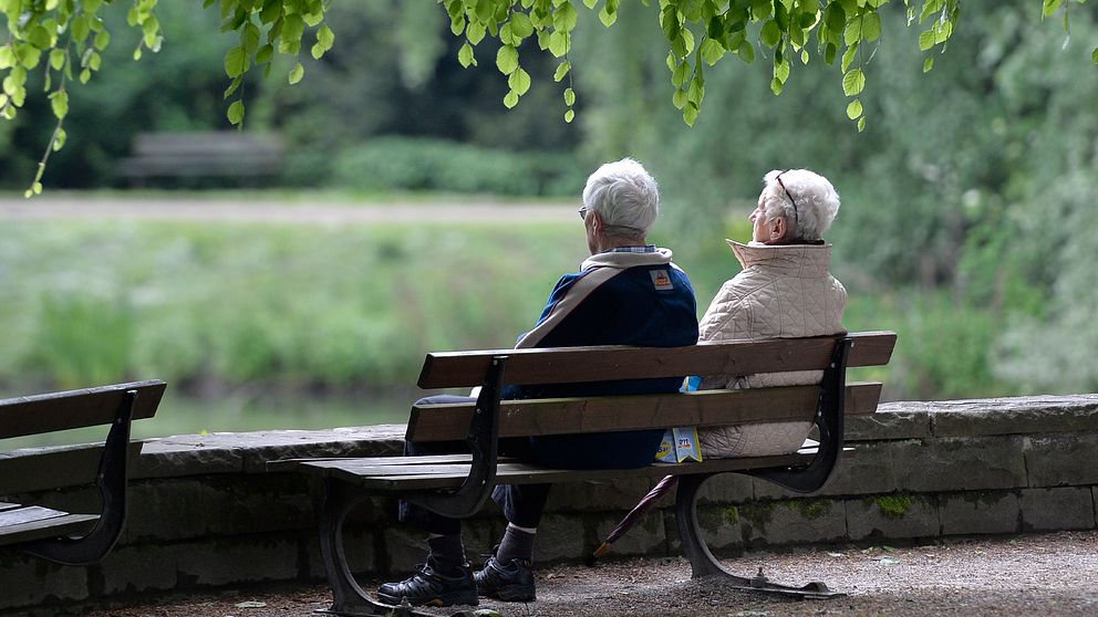 Äldre par sitter på en bänk i en park.