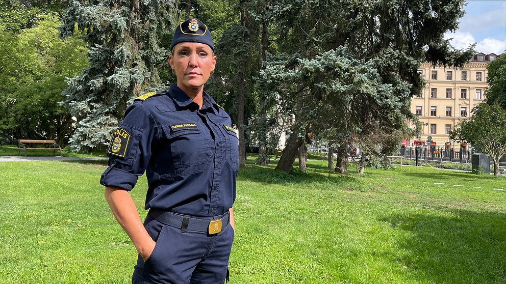 En kvinnlig polis som ser allvarlig ut i en solig park med träd i bakgrunden
