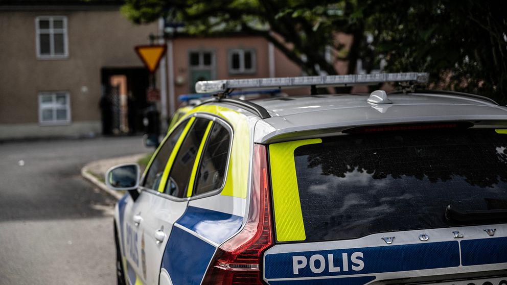 Polisbil fotad bakifrån framför några hus och en vägskylt. Sölvesborg, misshandel, Västra Storgatan.