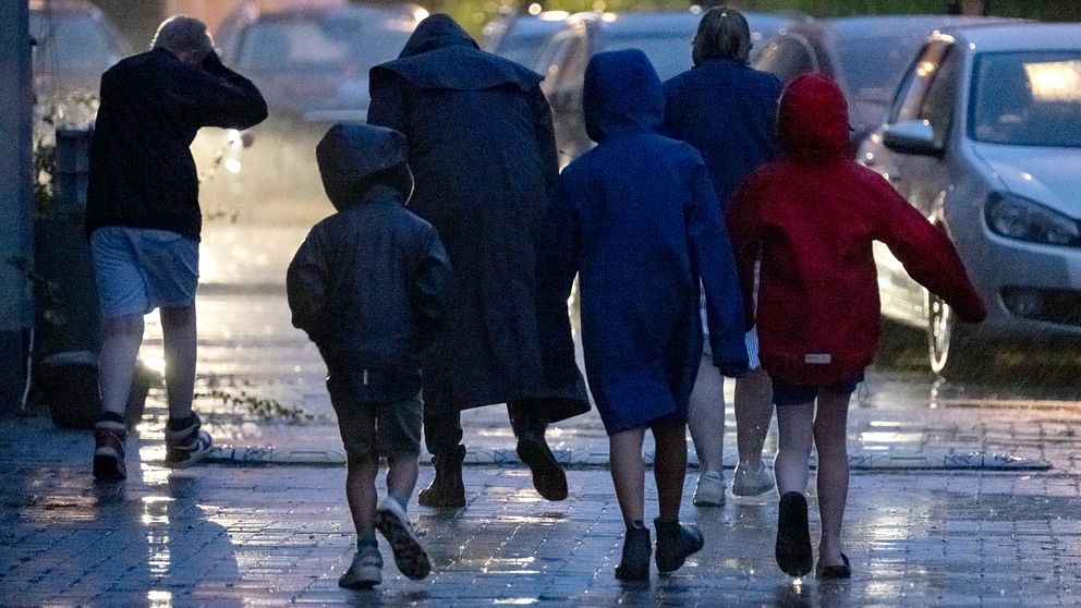 Folk i regnkläder på trottoar i blåst och regn.