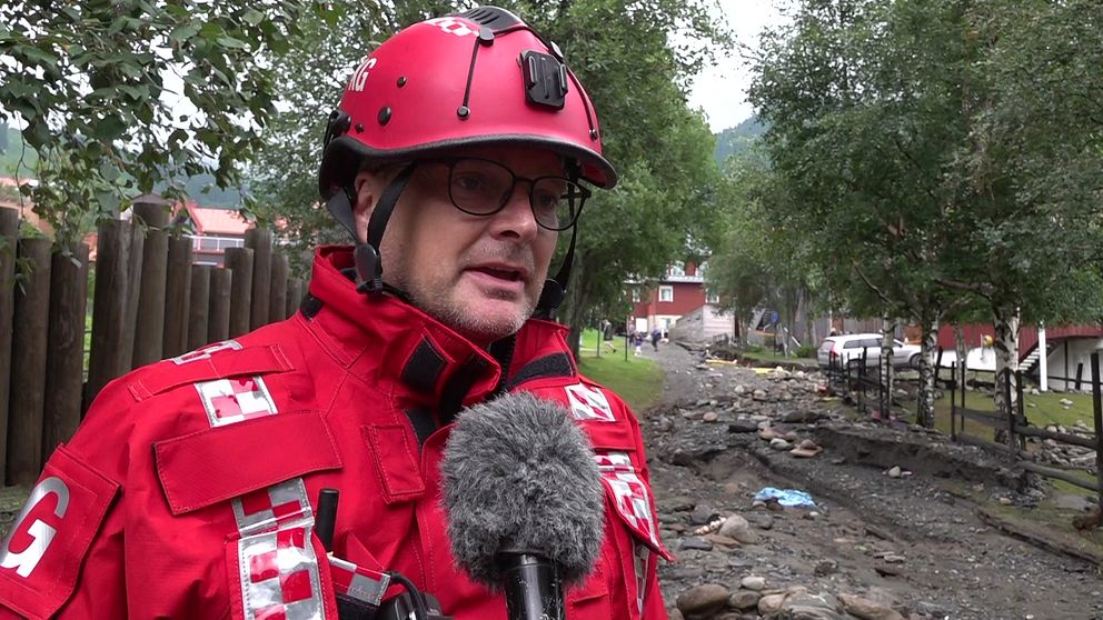 Räddningsledare Karl Groves på plats vid Susabäcken i Åre, med röda räddningskläder. Bakom honom syns förödelsen på platsen.