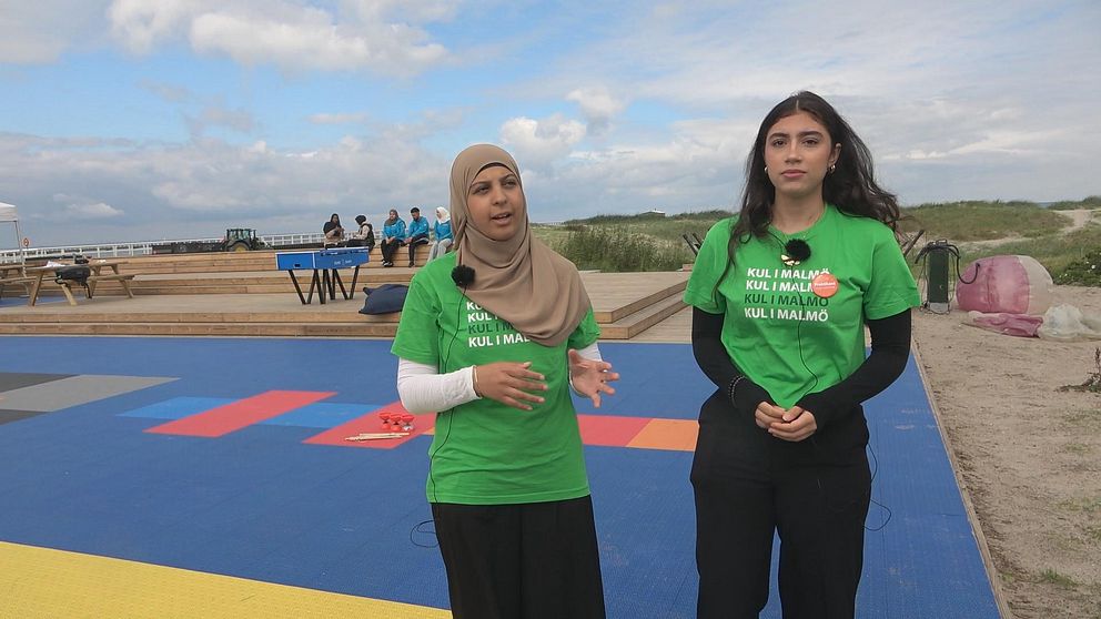 Två tjejer i gröna t-shirts som står vid en strand.