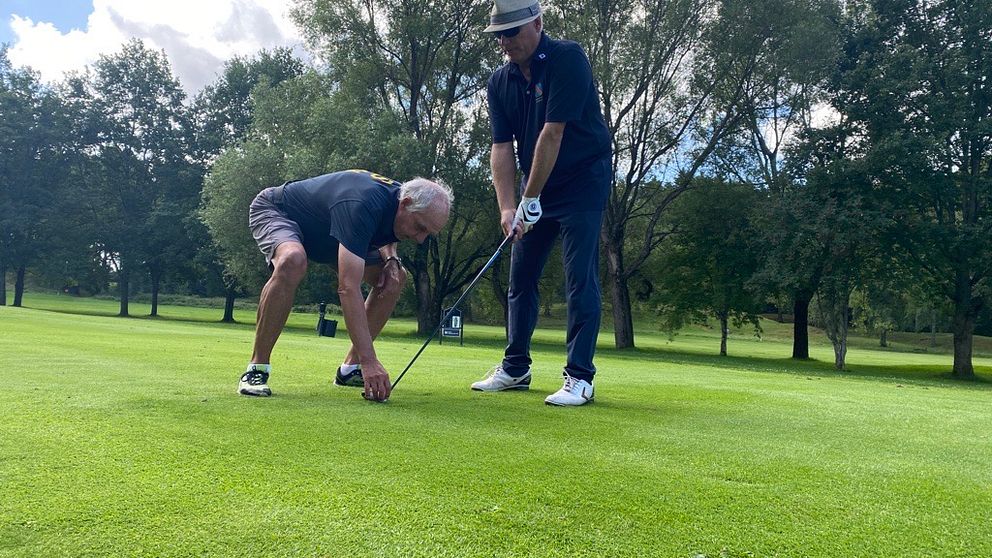 Två män spelar golf, en caddie visar en synskadad man hur han ska placera klubben för att få en bra träff