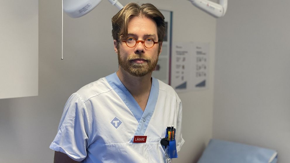 Läkaren Jonas Stenberg står i ett sjukhusrum i vita sjukhuskläder.