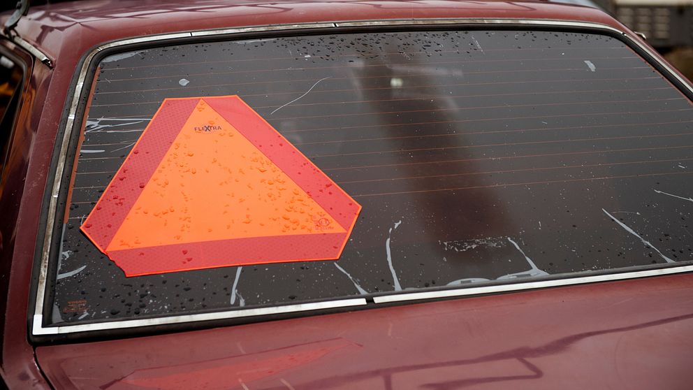 Baksidan av en bil med en röd-orange varningstriangel på bakrutan.