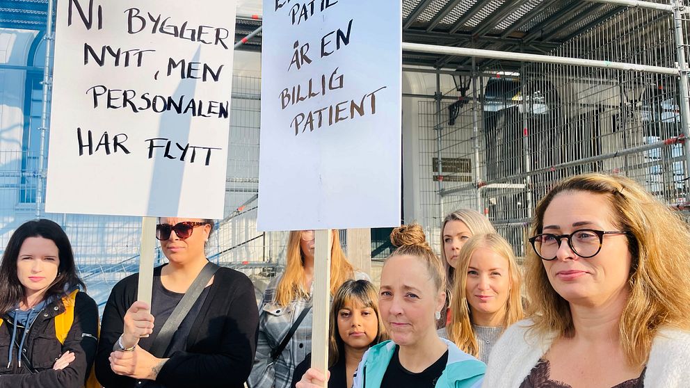 Läkare, sjuksköterskor och undersköterskormed plakat med texten ”Ni bygger nytt, men personalen har flytt” och ”En död patient är en billig patient”.