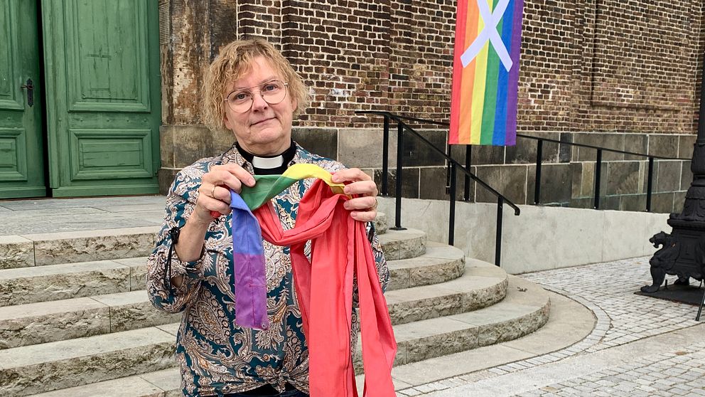 Kyrkoherden Eva-Lotta Grantén håller upp en del av en bränd regnbågsflagga utanför Sofia Albertina kyrkan.