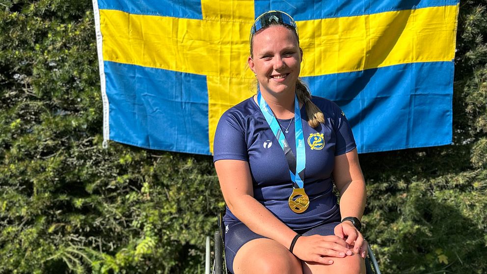 En parakanotist sitter i en rullstol framför svenska flaggan. Runt hennes hals hänger en guldmedalj.