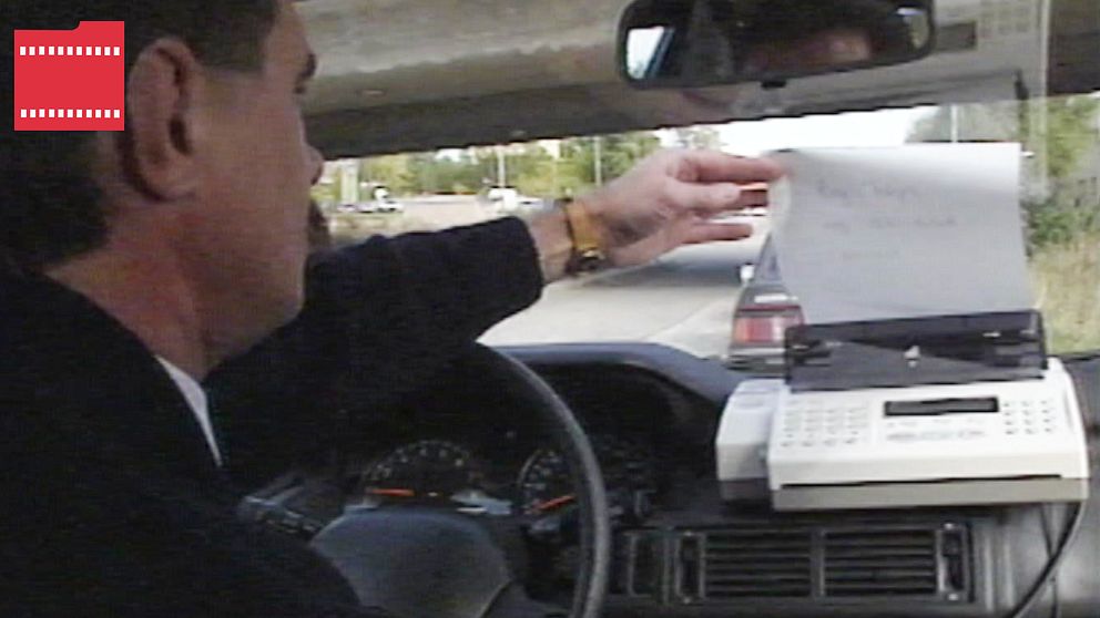 En man som tar ett papper från faxmaskin i en bil.