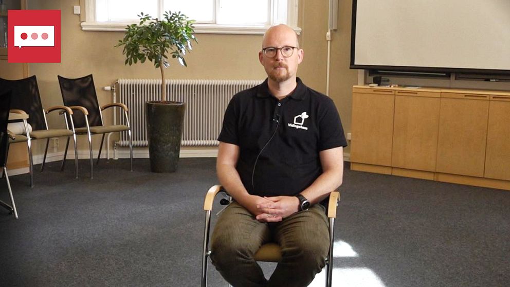 En man i bruna chinos, svart piké sitter på en stol i ett konferensrum. Han heter martin eneborg