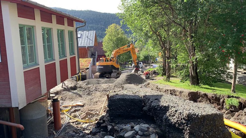 Bild från Åre by som drabbades av stora översvämningar under ovädret Hans. Ett hus som till synes hänger i luften och en grävmaskin som fyller i de djupa eroderingarna.