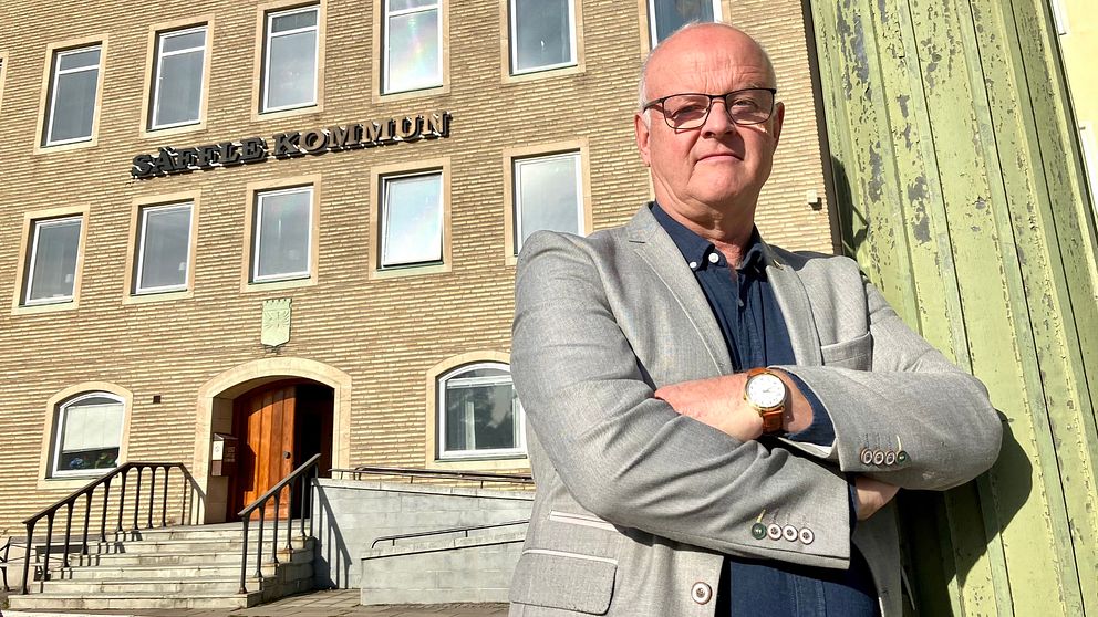 En man i ljusgrå kavaj och blå skjorta står med armarna i kors framför Säffles kommunhus.