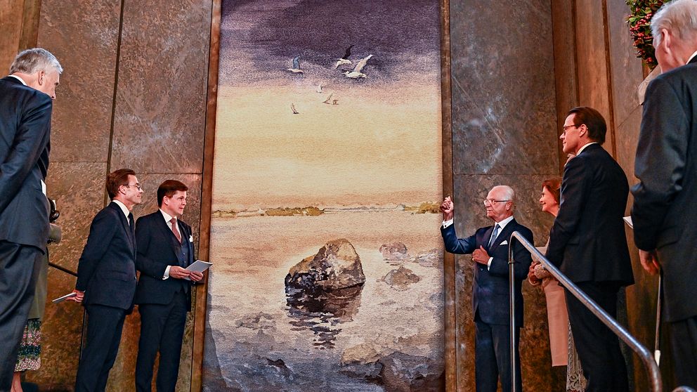 Sex män  och en kvinna står framför en vävd tavla föreställande Sten i vatten – ursprungligen en akvarellmålning av Lars Lerin.