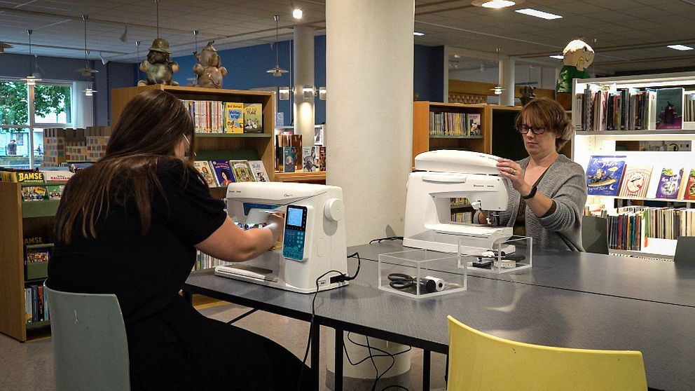Två kvinnor sitter vid symaskiner i ett bibliotek.