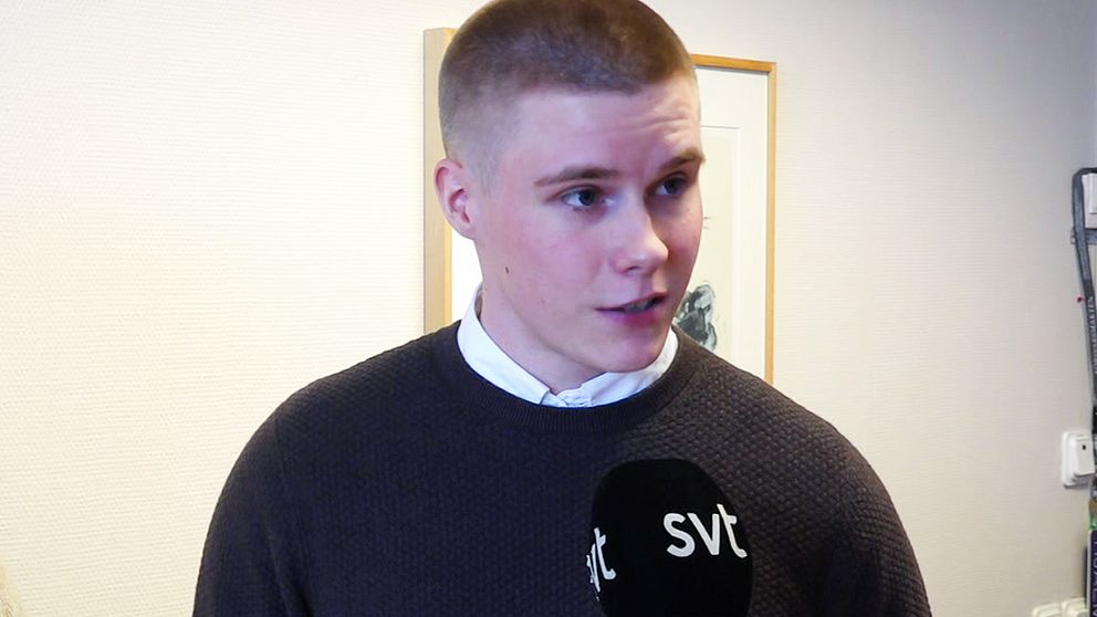 en korthårigman står i en brun tröja framför en vit vägg.