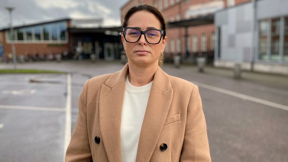 Lisa Bertilsson i glasögon och beige kappa framför akutmottagningen i Lidköping