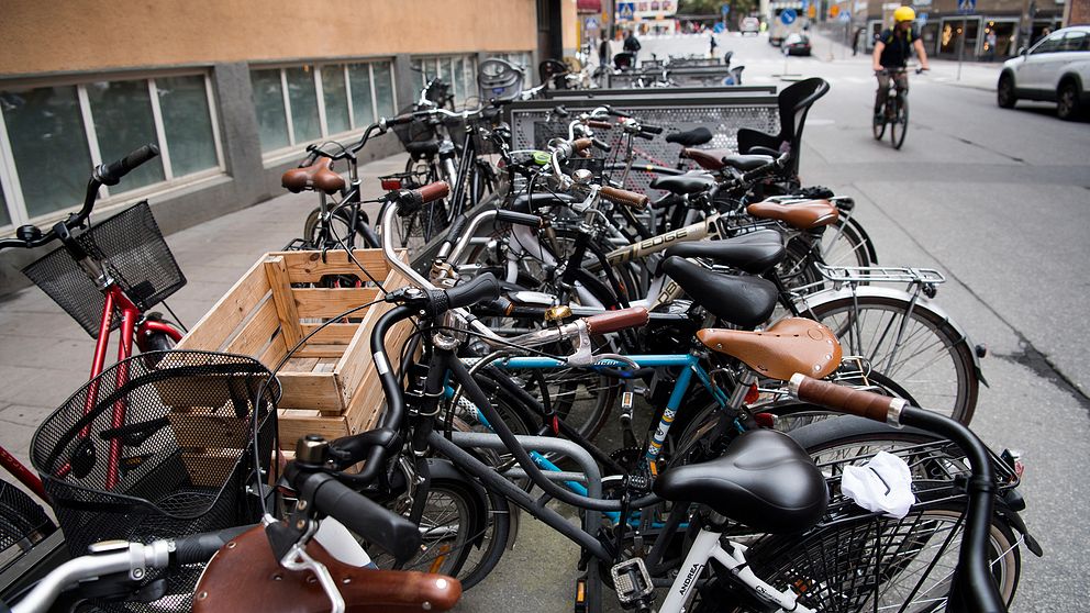 Flertalet cyklar står uppställda vid en trottoar.