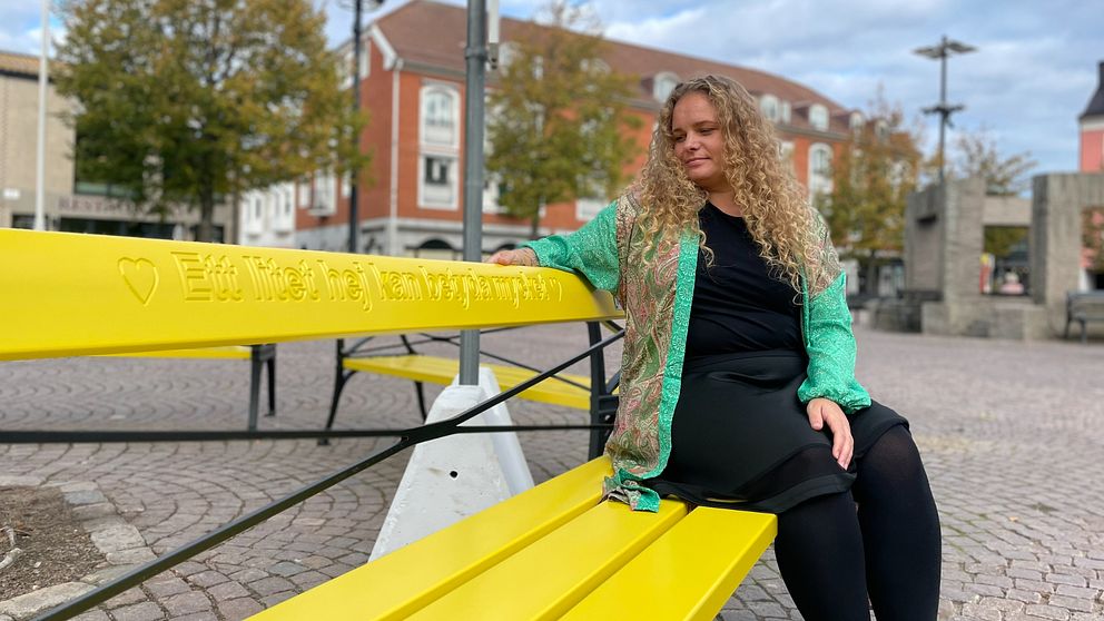 Sara Gigja, psykiatrisamordnare i Ängelholms kommun, sitter på en av de gula vänskapsbänkarna på Stortorget i Ängelholm.