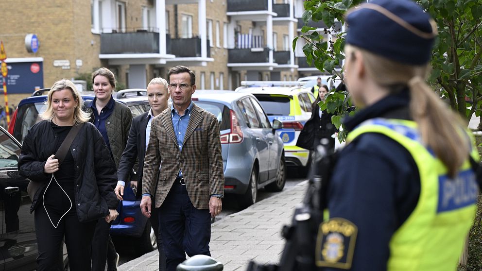 Statsminister Ulf Kristersson och hans medarbetare går på gatan i Malmö på väg mot synagogan. I förgrunden en beväpnad polis.