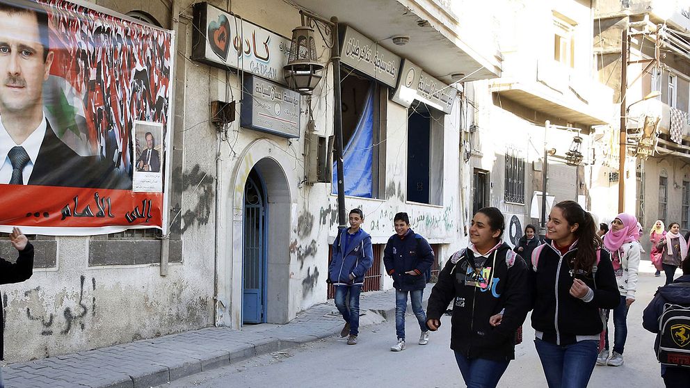 Skolelever passerar framför en affisch på Syriens president Bashar al-Assad i Homs, som nu åter kontrolleras av landets regering.