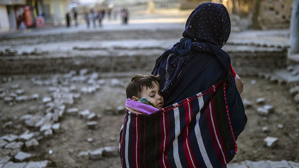 En kvinna bär på sitt barn och vandrar förbi barrikaderna i staden Nusaybin i sydöstra Turkiet.