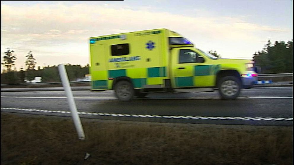 ambulans kör längs väg med skog bakom