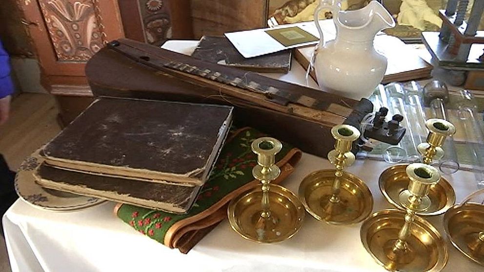 Antika föremål som ljusstakar och kyrkoskrifter på ett bord i Ytterhogdals hembygdsgård