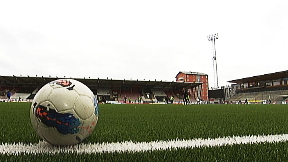 Fotboll på en gräsplan med lag i bakgrunden. Arena.
