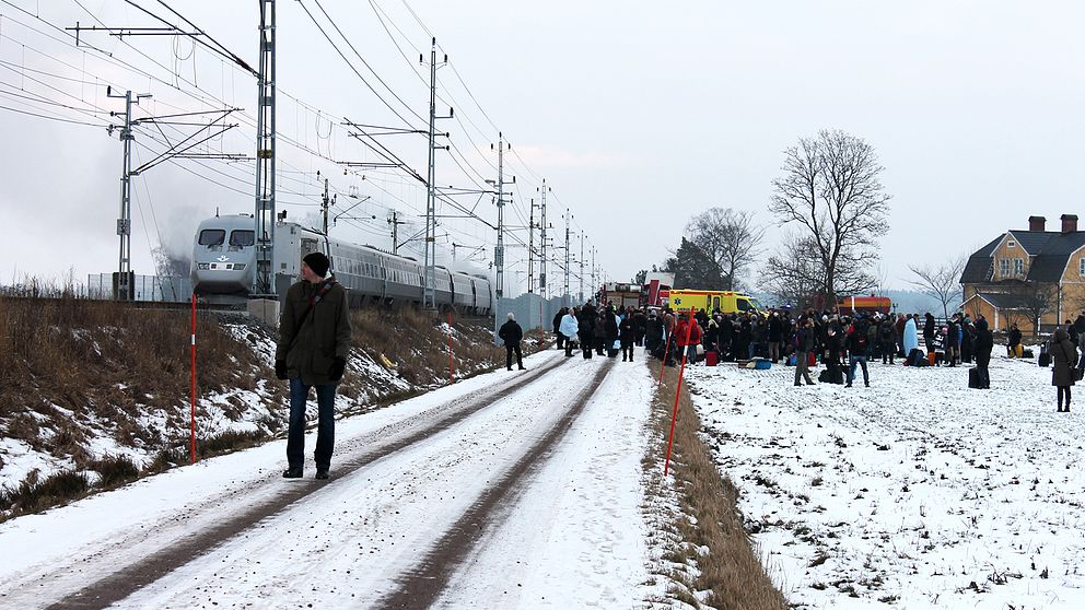 Evakuerade människor på ett gärde i snön. Tåg som ryker. Ambulans och räddningstjänst.