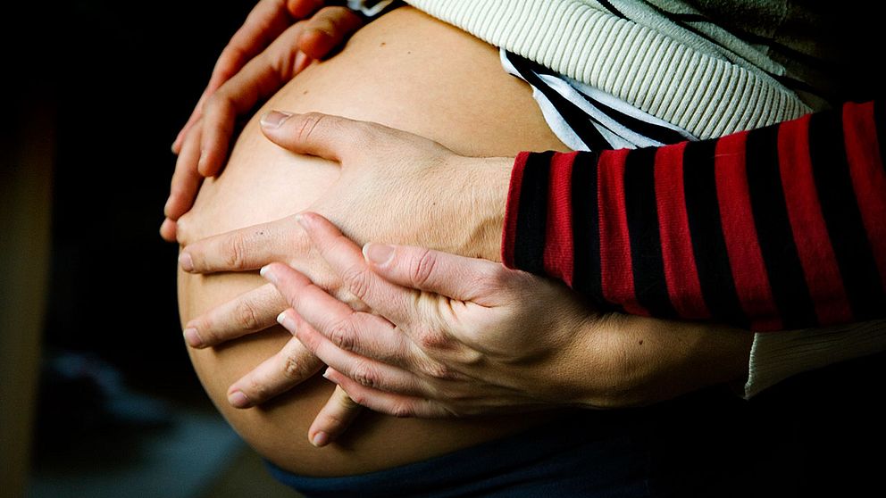 Gravid kvinna med händer på sin mage.