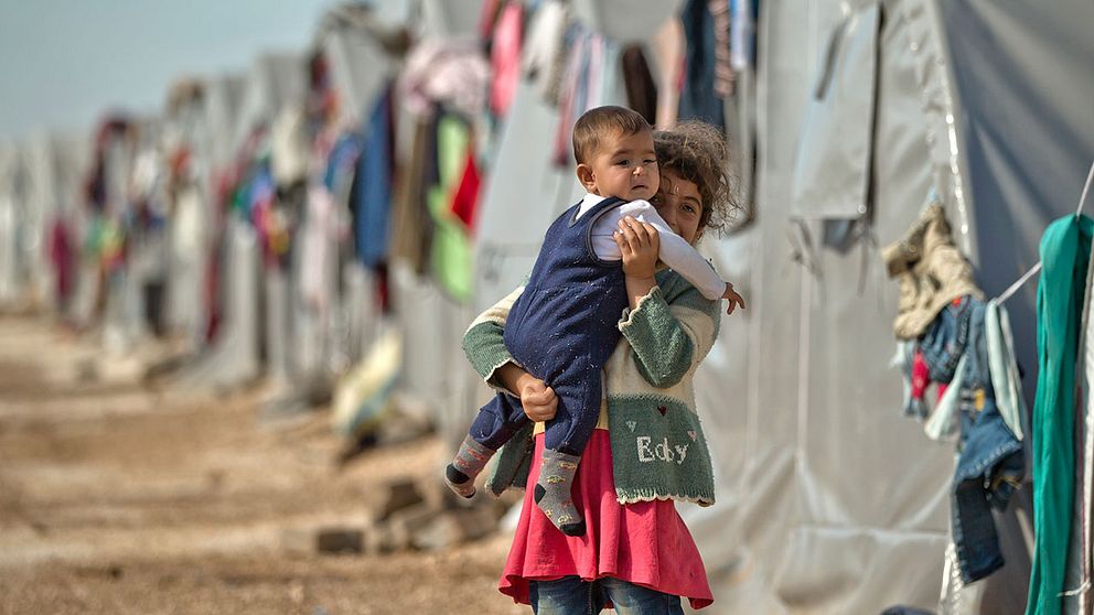 En syrisk flicka bär en baby i ett flyktingläger i Turkiet.