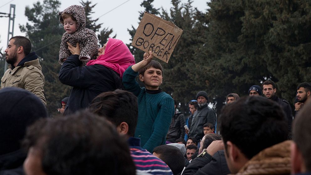 Flyktingar håller upp en skylt med texten ”Open border”.