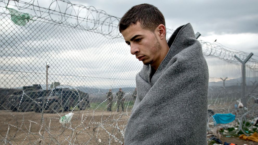 En ung man vandrar längs stängslet mellan Grekland och Makedonien, i närheten av gränsövergången Idomeni, där uppemot 14 000 personer väntar samtidigt som EU-ledarna möts.