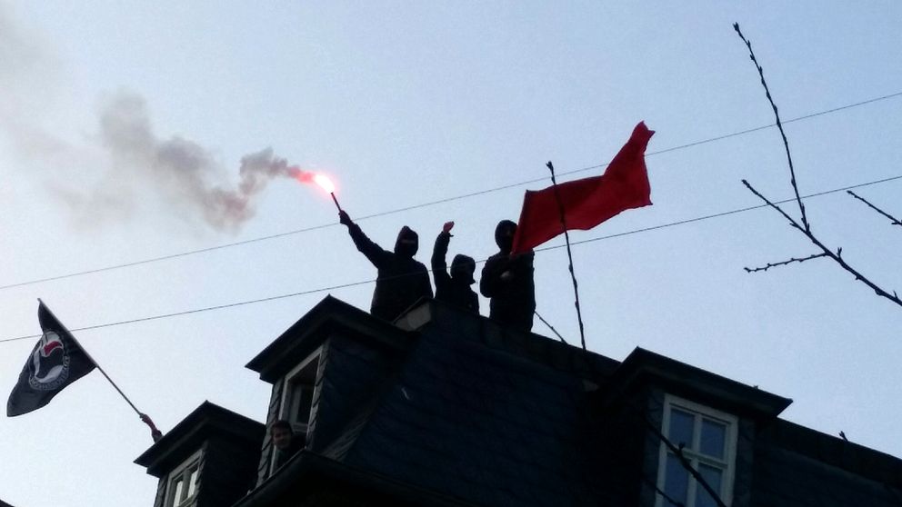 Motdemonstranter står på ett tak och har tänt pyroteknik.