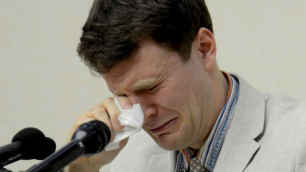 Otto Warmbier gråter under presskonferensen som sändes i statlig nordkoreansk tv i februari. Han håller en pappersnäsduk framför ansiktet. Framför sig har han tre mikrofoner.