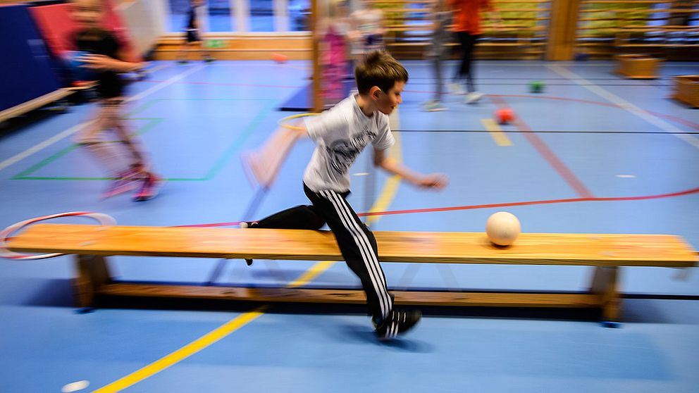 Pojke springer med boll i gymnastiksal.