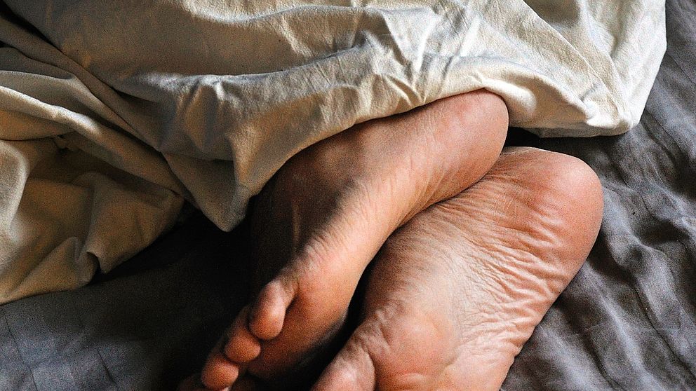 Fötter på person som ligger under täcke