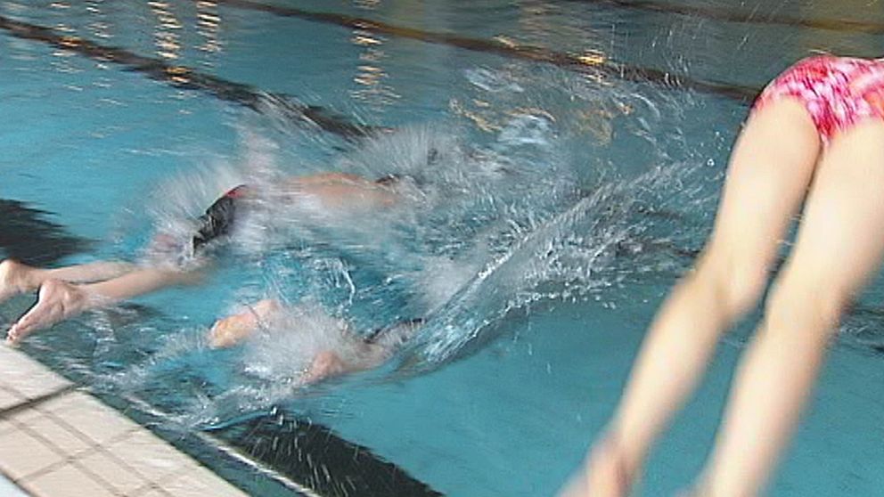 Barn som dyker i simbassäng i simhall.