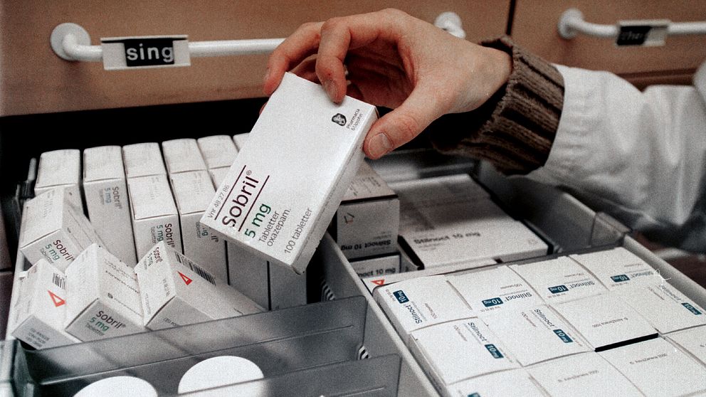 En hand lyfter ut ett paket antidepressiva, sobril, från en hylla på apoteket.