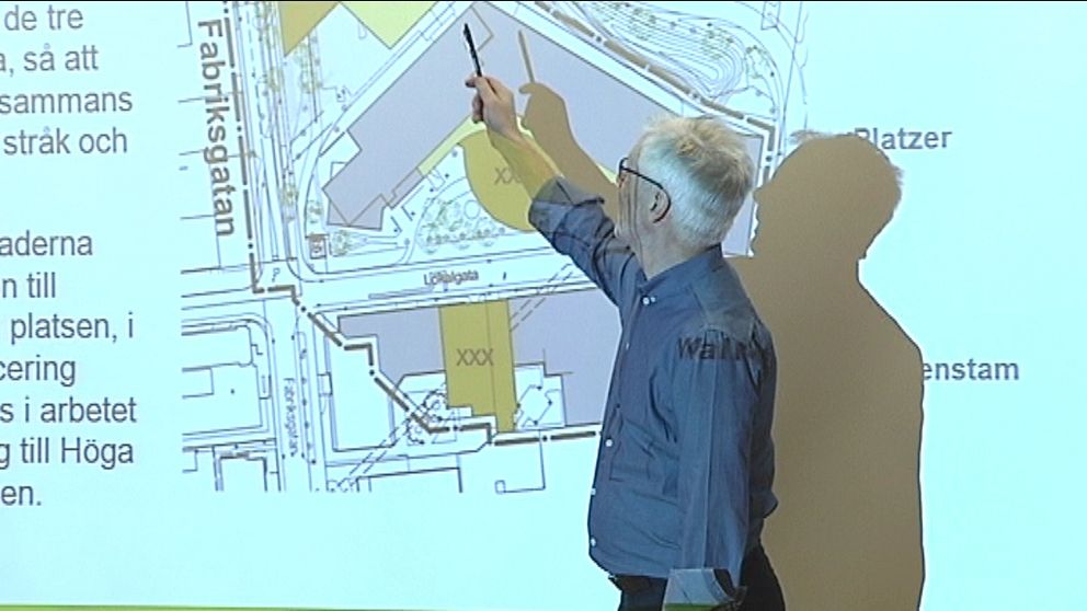 En man står framför en karta av området och pekar ut var husen ska byggas.