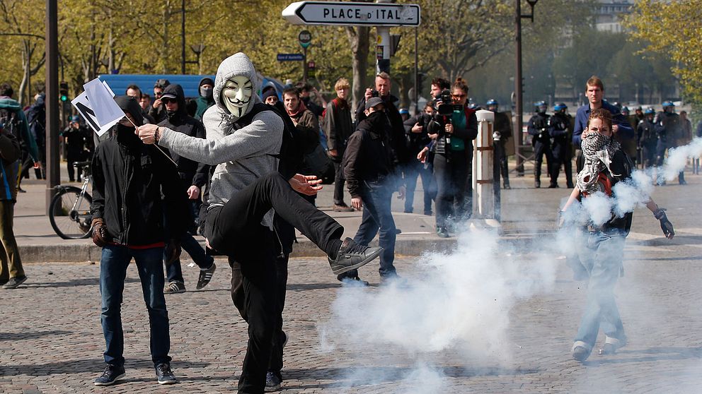 En maskerad demonstrant sparkar till en tårgasbehållare.
