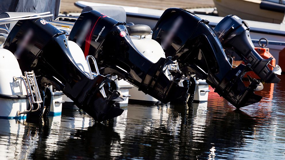 Svarta båtmotorer hänger på rad från båtar.