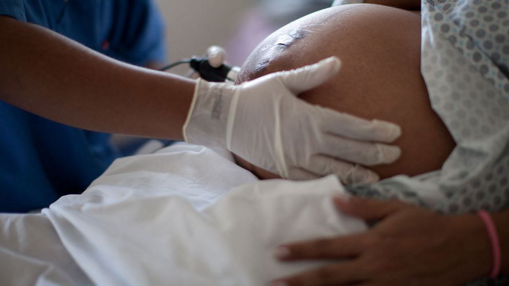 Gravidmage och sjukvårdspersonal som håller hand och instrument på magen