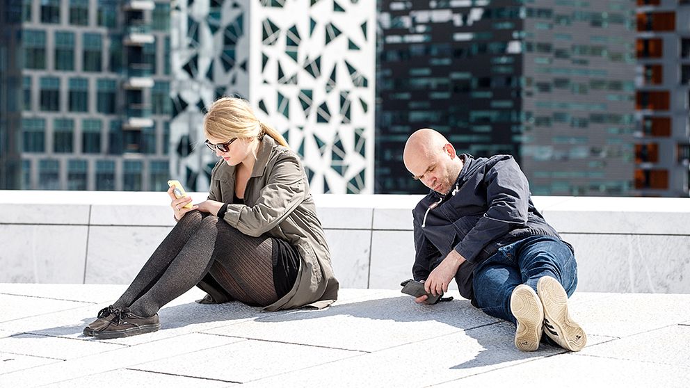 Kvinna och man sitter bredvid varandra och tittar på varsin mobiltelefon.