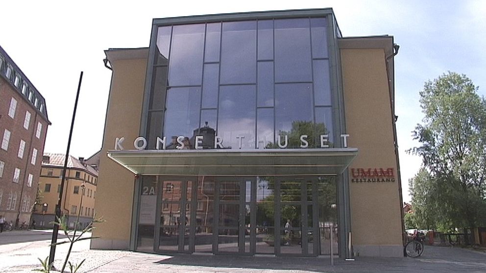 Entrén till Konserthuset med stora glasfönster och skylten ”KONSERTHUSET” i fronten, omgiven av grönska och stadsbyggnader i bakgrunden.