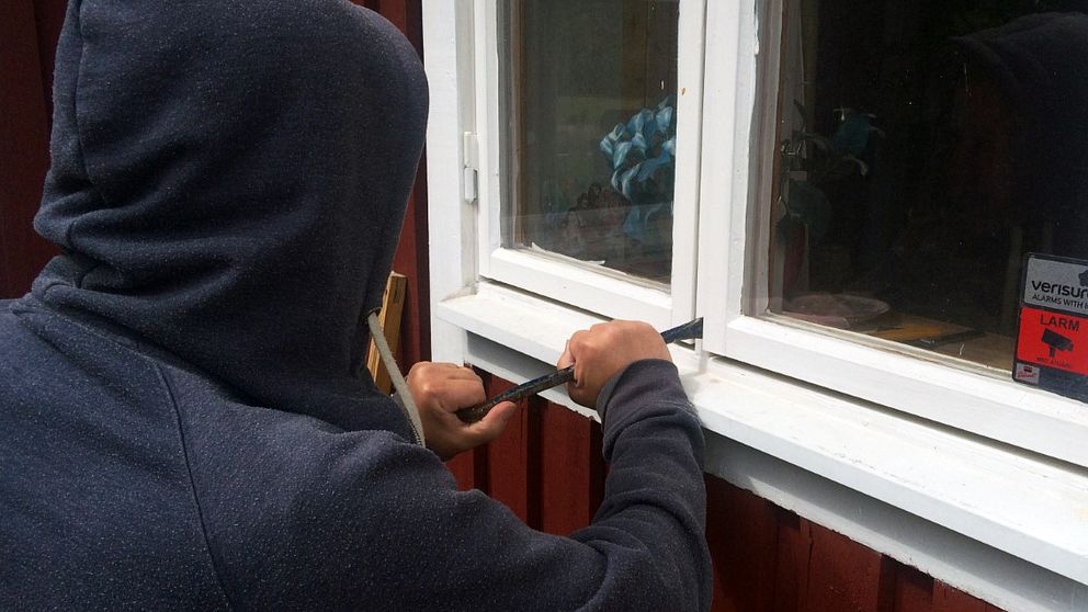 Anonym inbrottstjuv med huvtröja som har en kofot vid ett villafönster
