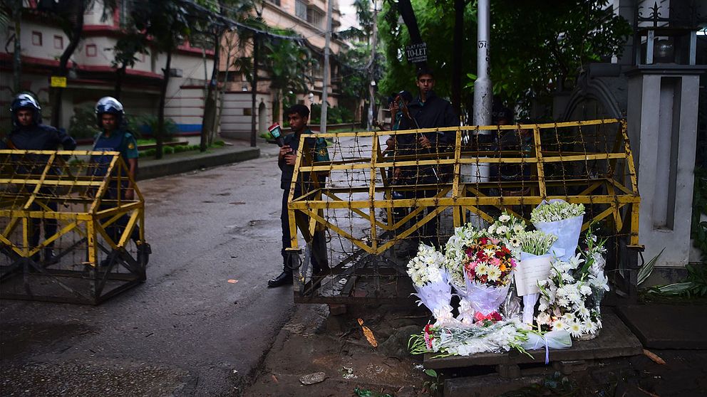 Polis och blommor vid vägspärr på vägen fram till den terrorutsatta restaurangen i Dhaka.