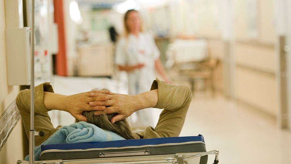 Patient ligger i på brits i sjukhuskorridor