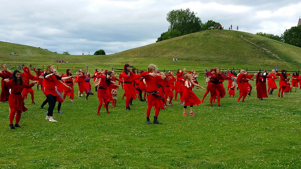 Ett hundratal rödklädda Kate Bush-fans dansar till tonerna av Wuthering heights med kungahögarna i Uppsala i bakgrunden.